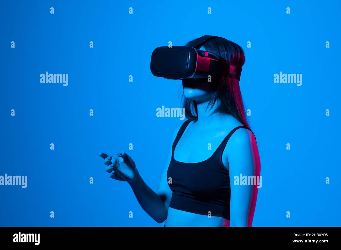 Jeune femme portant un appareil de réalité virtuelle dans une lumière de néon sur un fond bleu. Banque D'Images