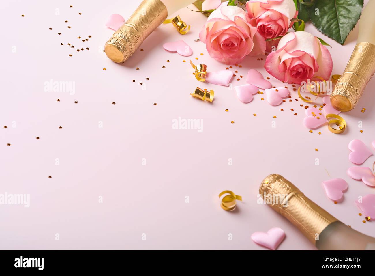 Roses roses fleurs, champagne, cadeau, rubans dorés et coeurs confettis rouges sur fond rose.Plan d'accueil avec vue de dessus et espace pour vos salutations.Valen Banque D'Images