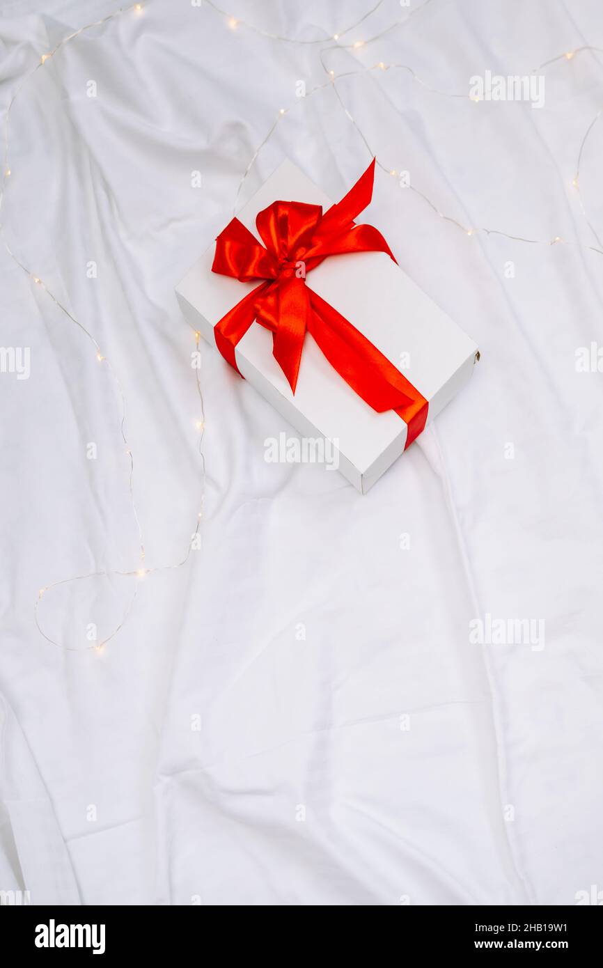 Boîte-cadeau blanche avec noeud rouge sur feuille blanche, vue du dessus.CopySpace Banque D'Images