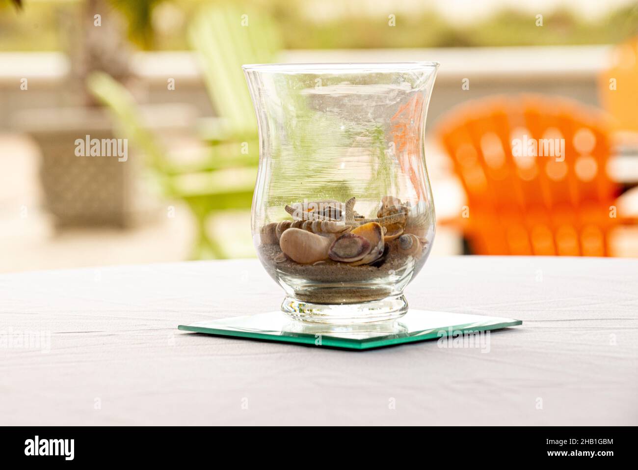Vase en verre pièce maîtresse remplie de coquillages sur table blanche à l'extérieur près de la plage Banque D'Images