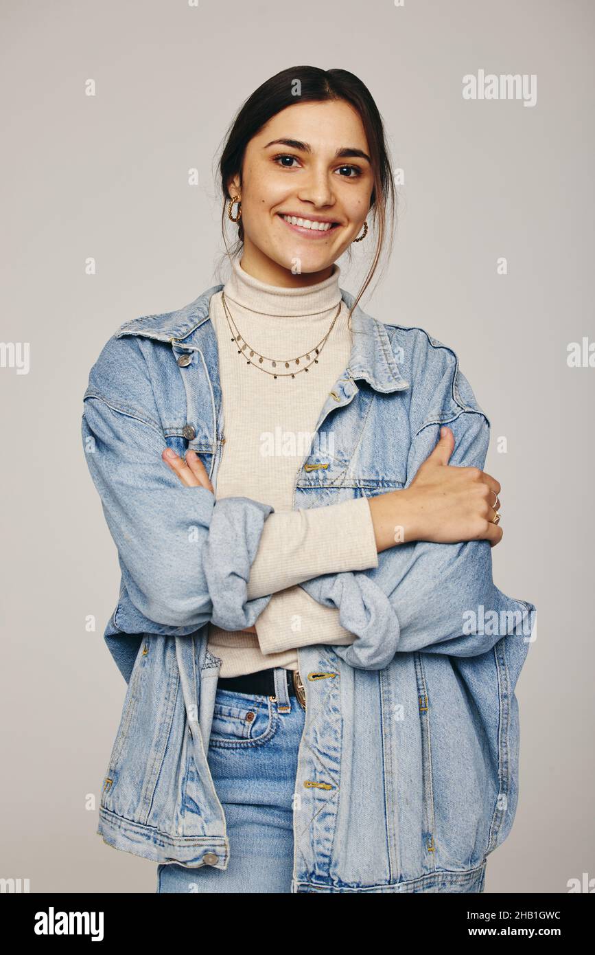 Jeune femme élégante souriant à la caméra tout en restant seule.Une jeune femme heureuse debout avec ses bras croisés sur fond gris.Elégant yo Banque D'Images