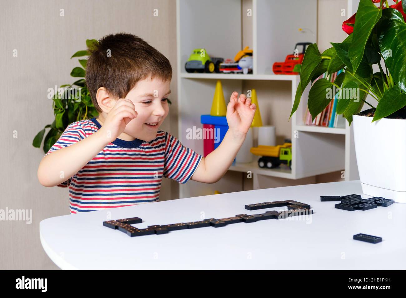 Un garçon heureux de 4 ans joue un jeu de dominos, s'amuse et aime le jeu. Banque D'Images