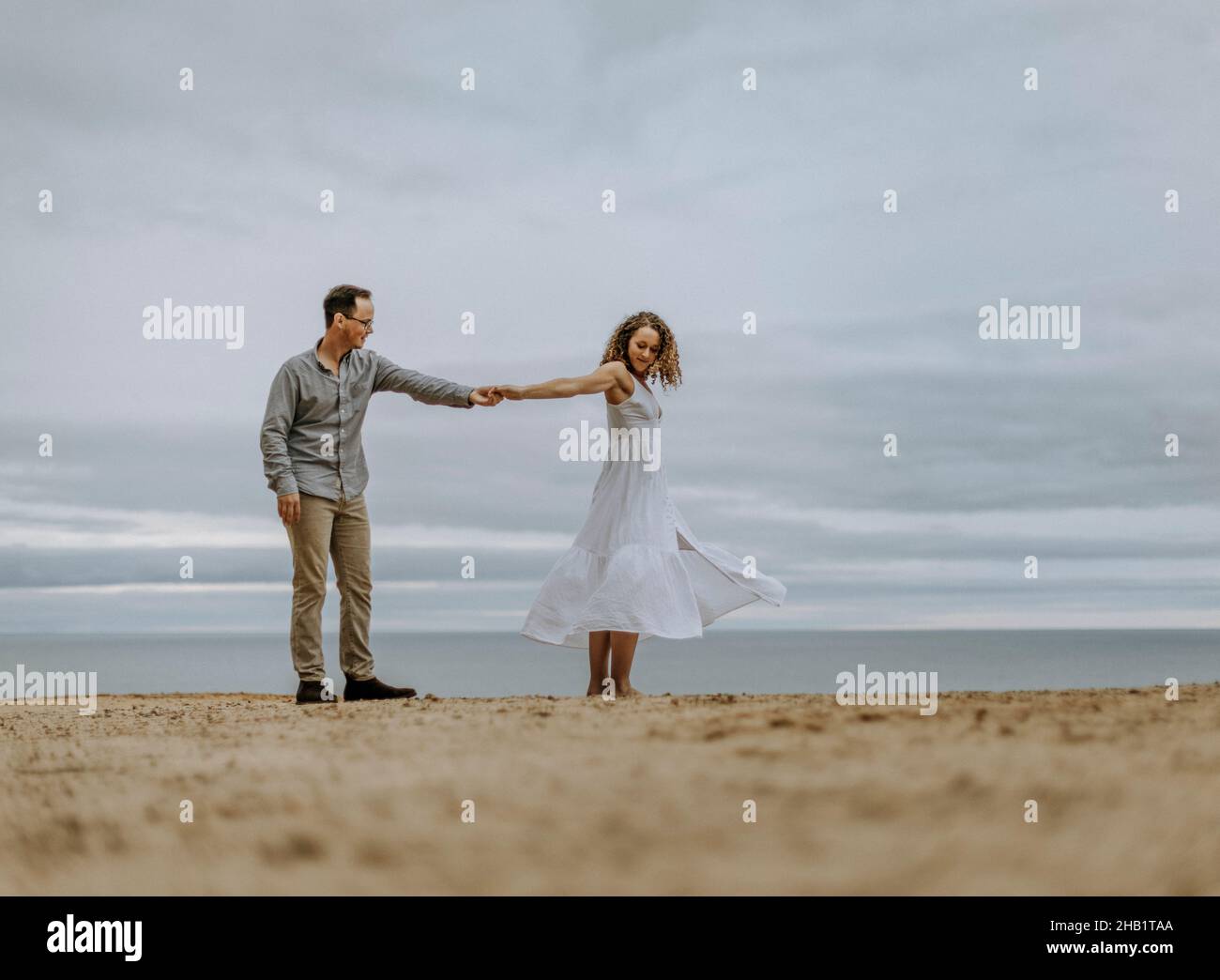 L'homme danse avec la femme en robe blanche sur la plage de sable à côté de l'eau Banque D'Images