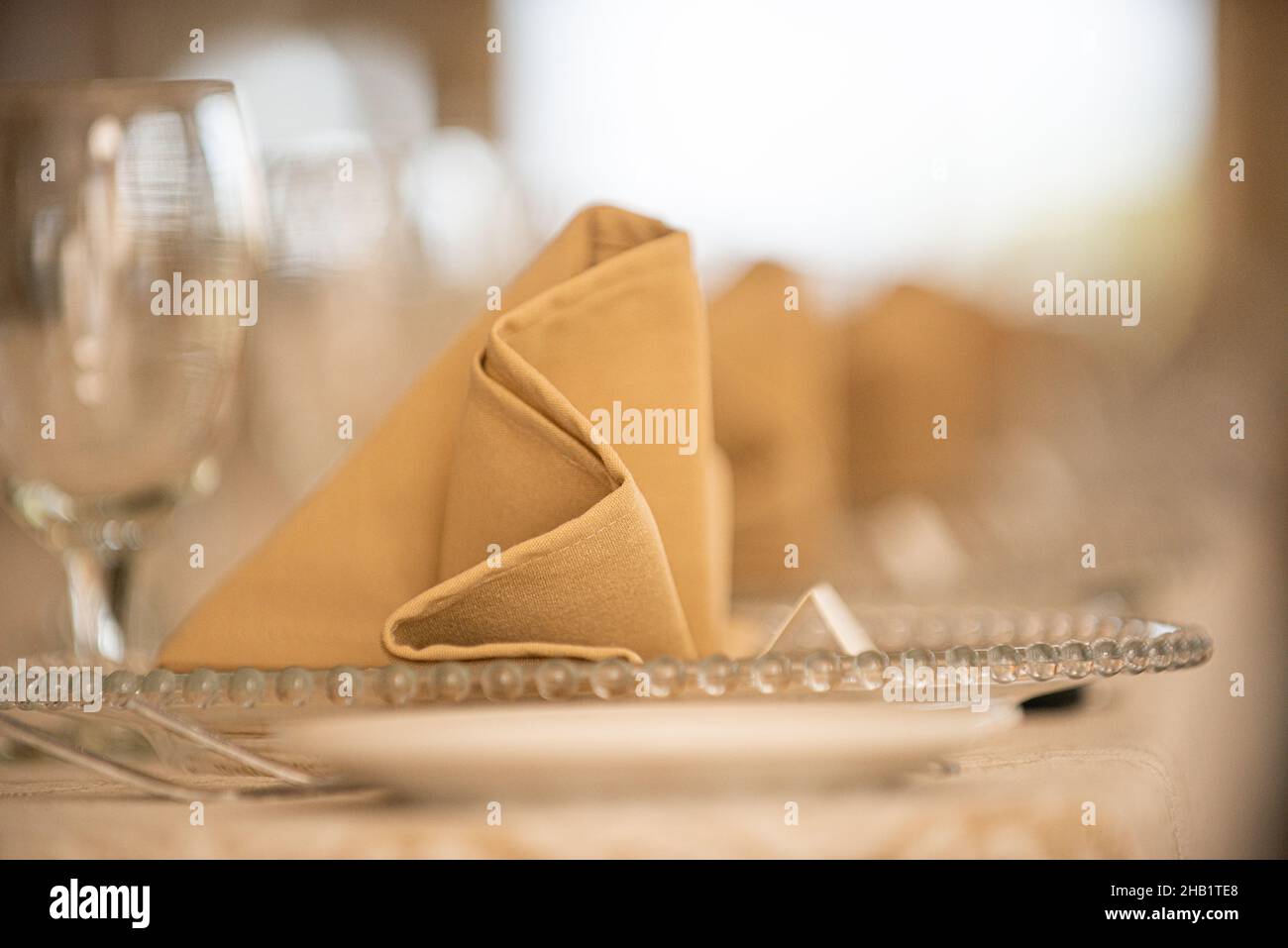 Des rangées de linge beige plient des serviettes de table sur des assiettes en verre lors du dîner Banque D'Images