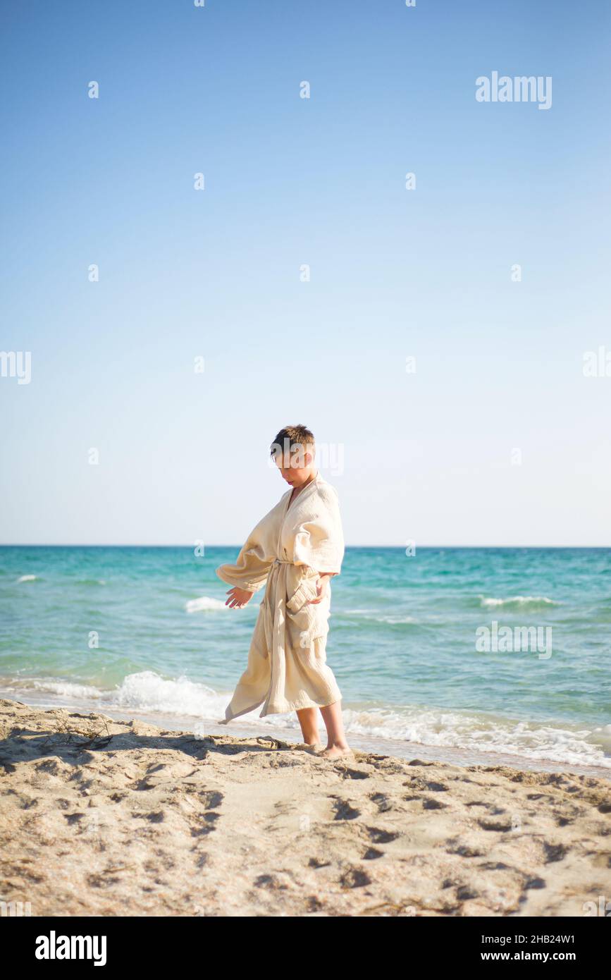 Pratique sur la plage.Un garçon dans une robe de mousseline sur le fond de la mer fait des exercices d'énergie. Banque D'Images