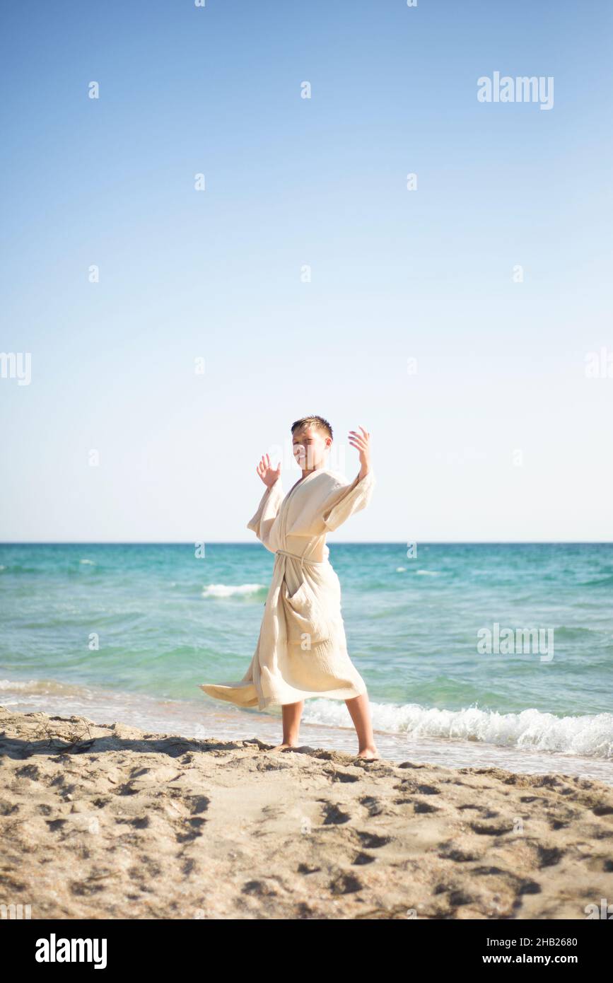 Pratique sur la plage.Un garçon dans une robe de mousseline contre le fond de la mer dans la pose d'un guerrier. Banque D'Images