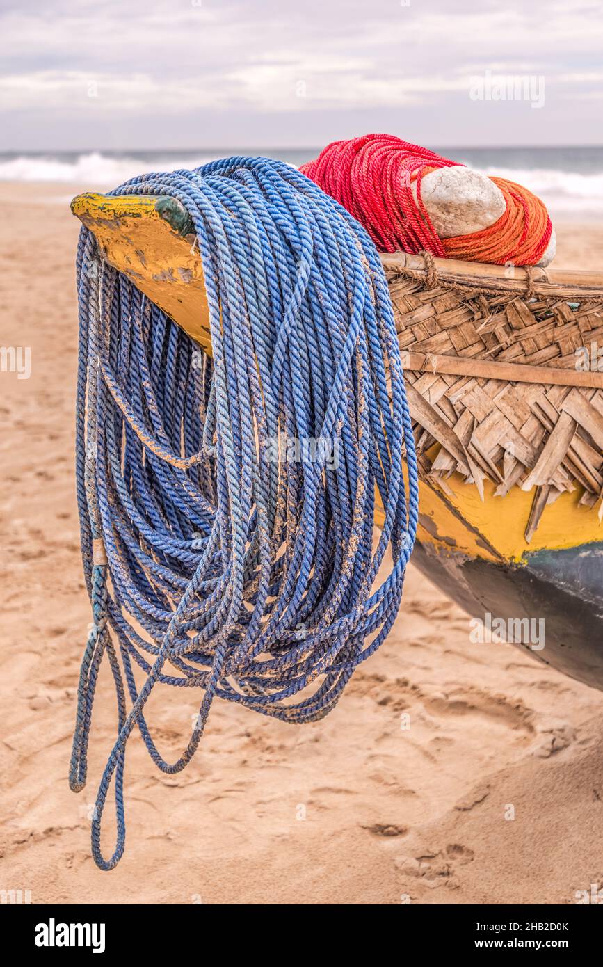 Gros plan d'une corde d'amarrage bleue et rouge attachée autour d'une poupe d'un bateau en bois de couleur jaune-bleu sur la plage. Banque D'Images