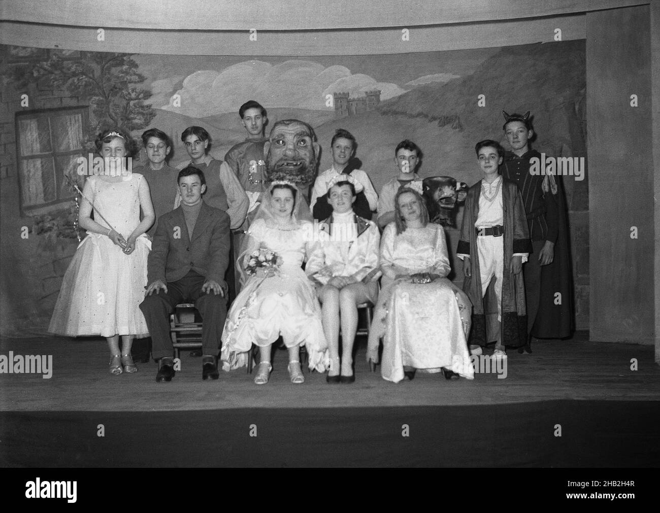 1956, historique, sur une scène en bois, la troupe de Jack et de la Beanstalk dans leurs costumes, se rassemblent pour une photo de groupe, Angleterre, Royaume-Uni.Publié pour la première fois en 1734 sous le nom de « l'histoire de Jack Spriggins et de The Enchanted Bean » - bien qu'il s'agisse d'un conte datant de plusieurs siècles avant cela - il s'agit d'une histoire populaire en anglais sur un garçon qui vend la vache familiale pour des haricots magiques, qui se transforme en une énorme manomantige,Où Jack monte où il rencontre un géant peu amical ou une orge.Dans le '50s, avant la télévision de masse, la dramatise amateur était une activité de loisir populaire pour les gens à prendre part à. Banque D'Images