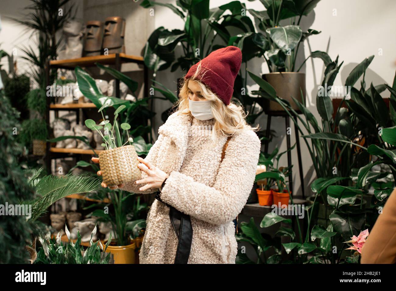 Jeune femme blonde en fausse fourrure, choix de la fleur en pot à la  boutique de fleurs, centre de jardinage, vie urbaine, style de vie,  Hobby,Reproduction de fleurs.Accueil gard Photo Stock -