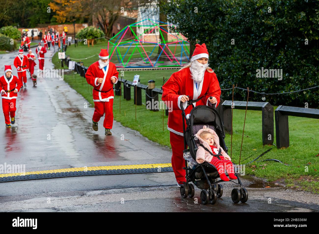 Femme en costume de Santa poussant la fille dans le buggy pendant un Santa Dash Banque D'Images