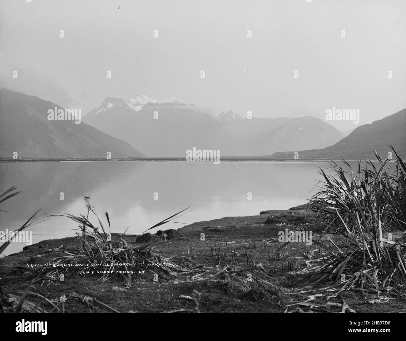 Mont Earnlsaw, de Glenorchy, lac Wakatipu, studio Burton Brothers, studio de photographie,1886, Dunedin, photographie en noir et blanc, vue sur les eaux mortes d'un lac vers les montagnes enneigées.Des amas de végétation déchiquetées sont visibles sur la rive de sable au premier plan Banque D'Images