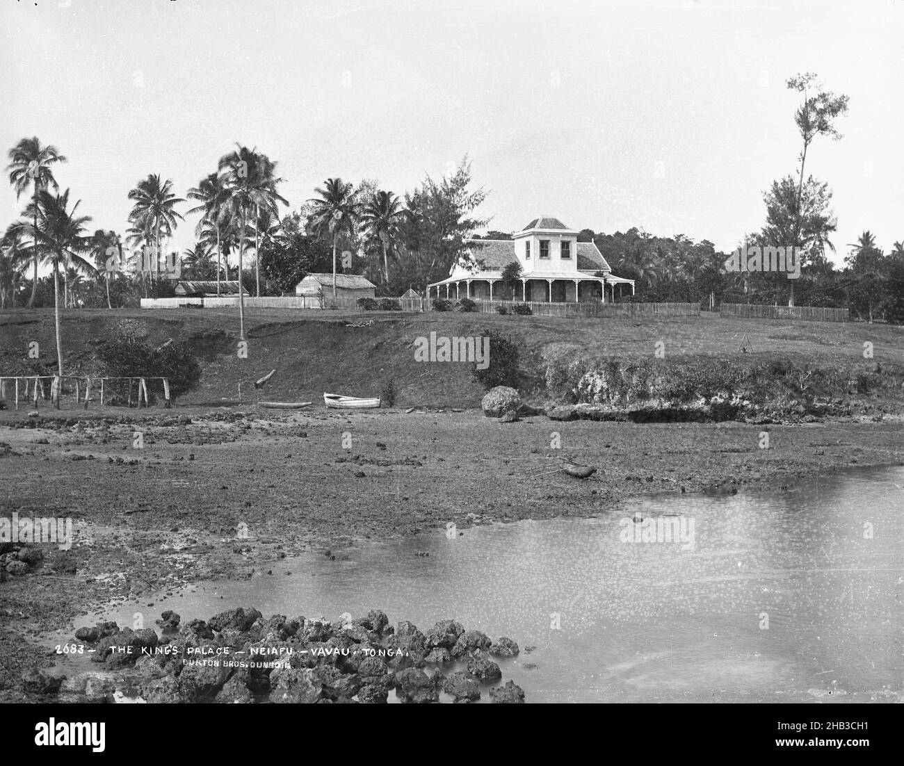 Le Palais du Roi, Neiafu, Vavau, Tonga, Burton Brothers studio,Studio de photographie, 1884 juillet, Nouvelle-Zélande, photographie en noir et blanc, estran des Rocheuses en premier plan, avec marée en sortie et bateau à rames au bas du centre de la banque.Hill Above a deux étages colonial bâtiment avec véranda au rez-de-chaussée et grande tourelle deuxième étage (centre).D'autres bâtiments à gauche et une clôture s'entour.Les cocotiers entourent Banque D'Images