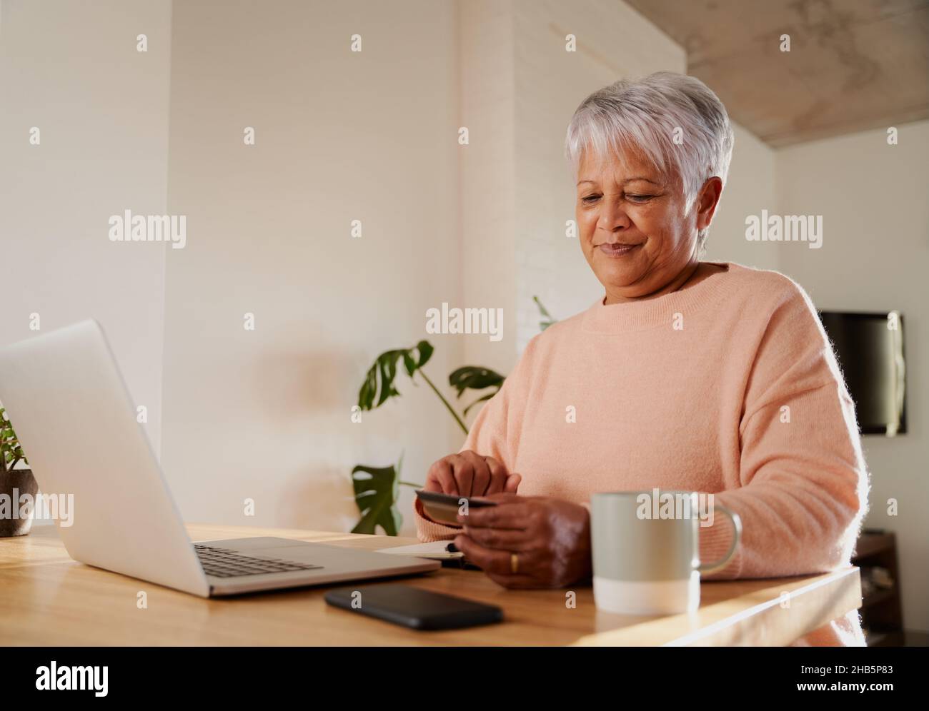 Une femme multiethnique âgée se fait un plaisir d'acheter en ligne sur un ordinateur portable, au comptoir de la cuisine. Banque D'Images