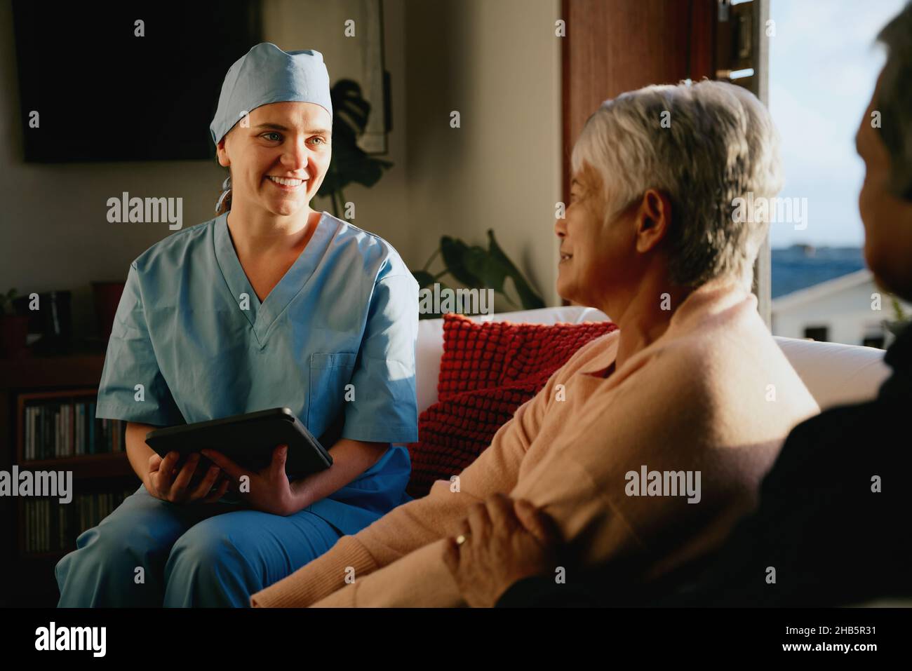 Professionnel de la santé souriant au couple multiethnique âgé.Consultation à la maison dans le salon moderne. Banque D'Images