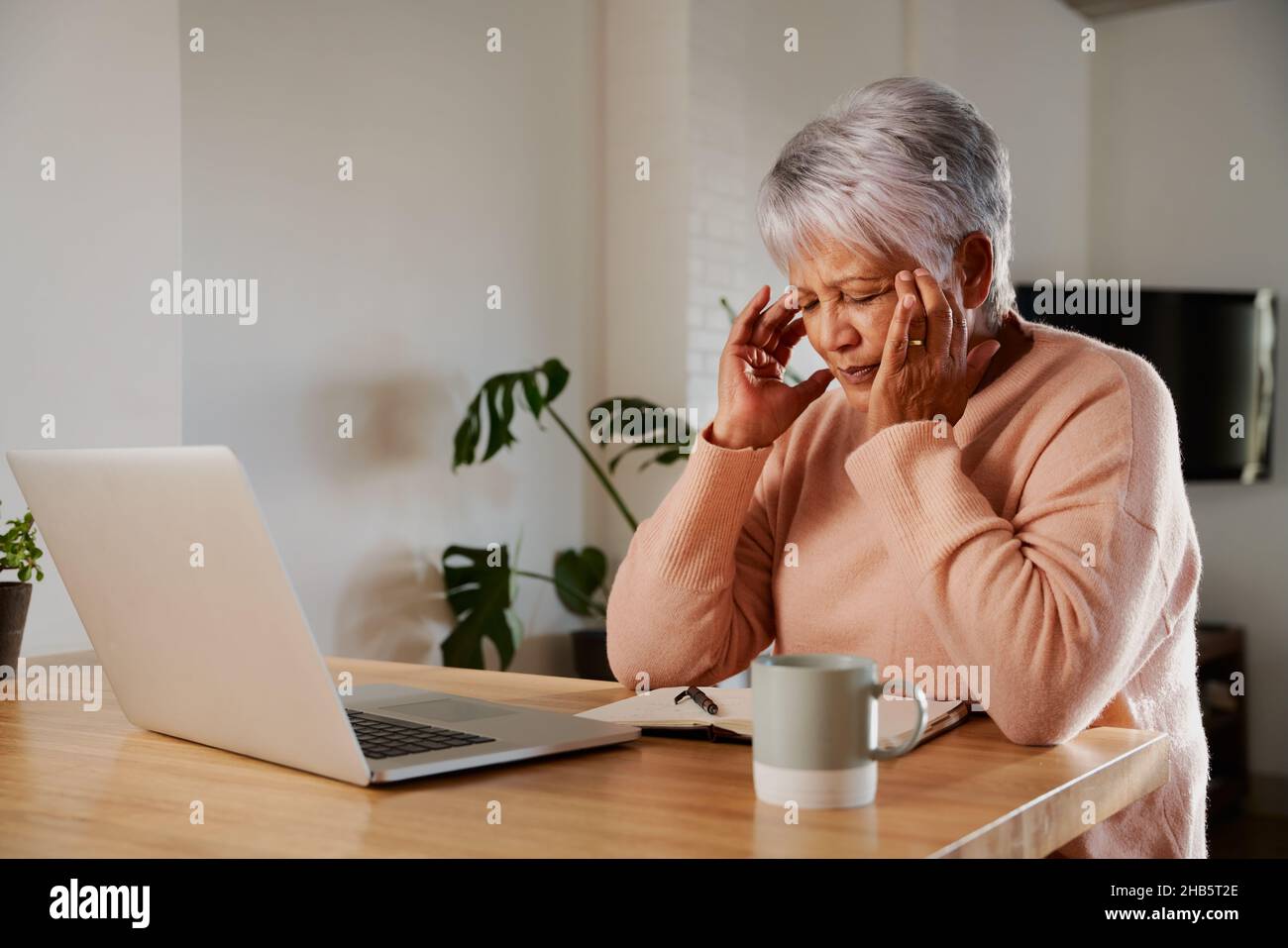 Une femme âgée multiethnique se tenant la tête dans la douleur.Asseyez-vous avec mal de tête au comptoir de cuisine moderne à la maison. Banque D'Images
