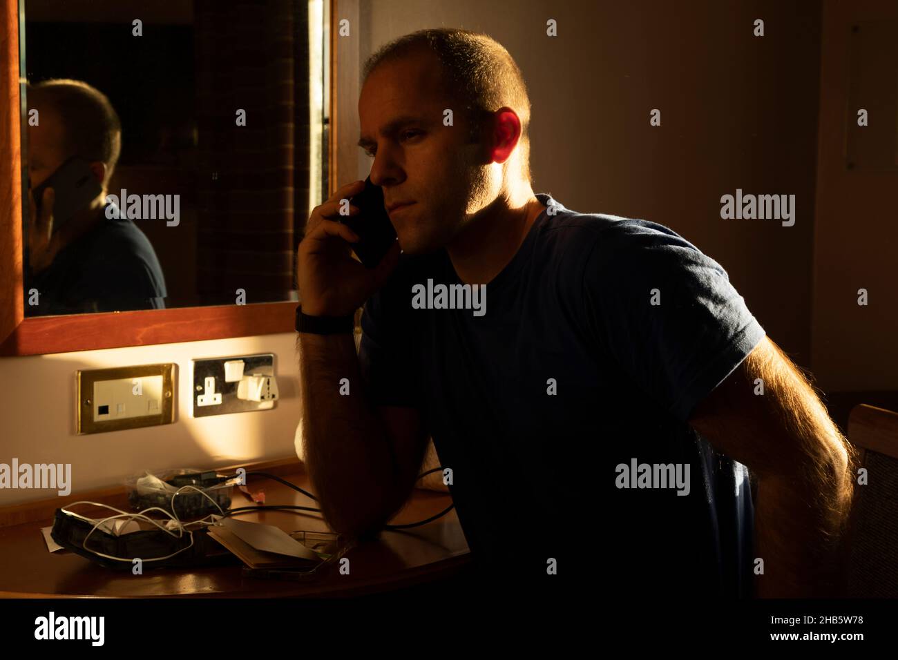 Un homme d'âge moyen appelle sur un téléphone mobile en attendant les résultats d'un test pcr Covid-19, auto-isolé, dans une chambre d'hôtel près de l'aéroport de Manchester, Banque D'Images