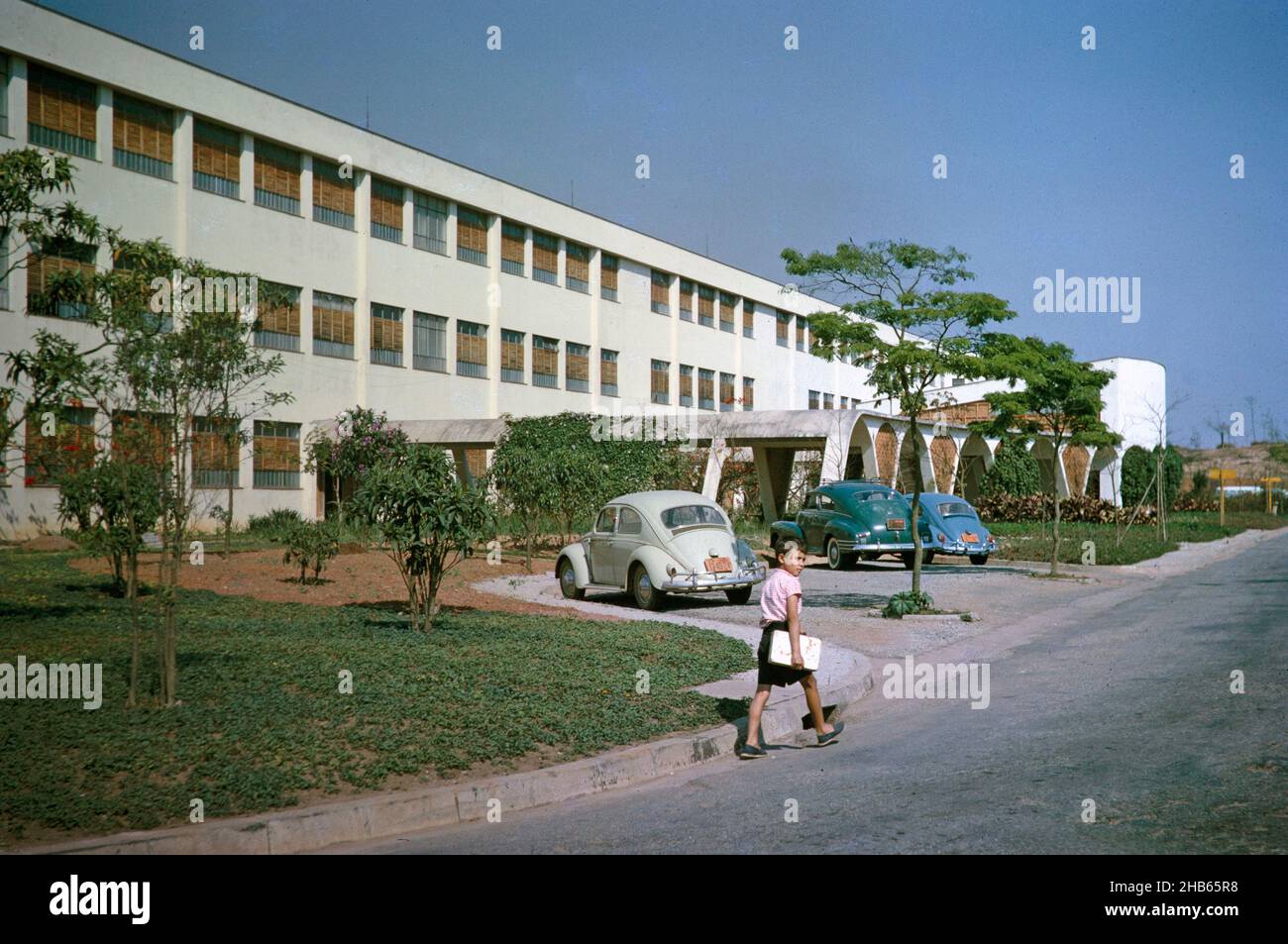 Jeune garçon marchant dans la rue VW Volkswagen Beetle voitures garées par le bâtiment de l'université, Sao Paulo, Brésil, Amérique du Sud 1962 Banque D'Images