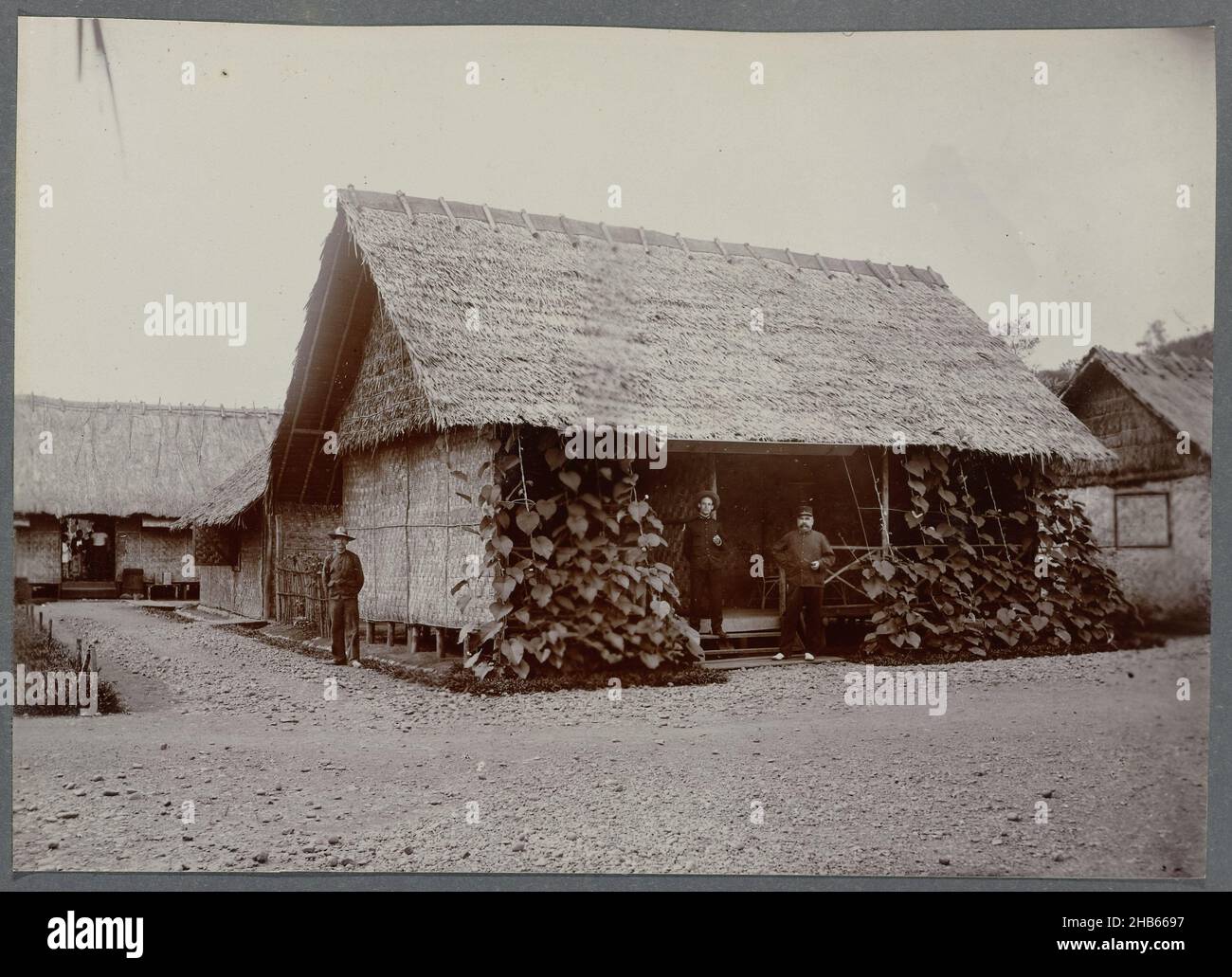 Bâtiment dans le bivouac à Krueng Seumpo, bâtiment dans le bivouac à Krueng Seumpo, deux officiers se tenant devant l'entrée.Photo encadrée dans un album avec 87 photos sur la construction de la route de Gajo sur le nord de Sumatra entre Bireuen et Takinguen entre 1903 et 1914., anonyme, Noord-Sumatra, 1903 - 1913, support photographique,hauteur 138 mm × largeur 200 mm Banque D'Images