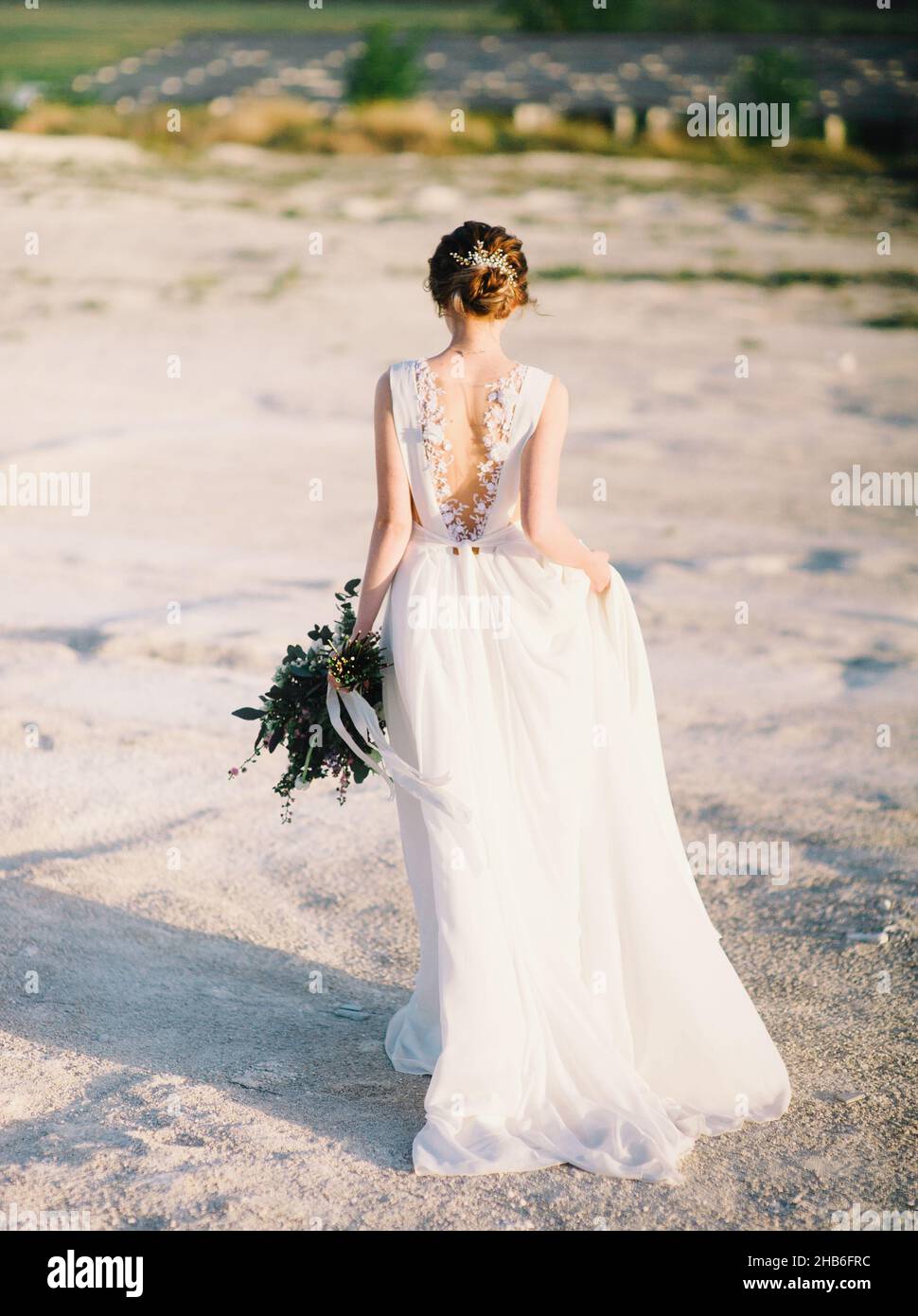 Mariage dans le désert, coucher de soleil, heure d'or.Yong mariée en robe de dentelle blanche va dans le désert et gardant le bouquet de mariage avec des fleurs tendres. Banque D'Images