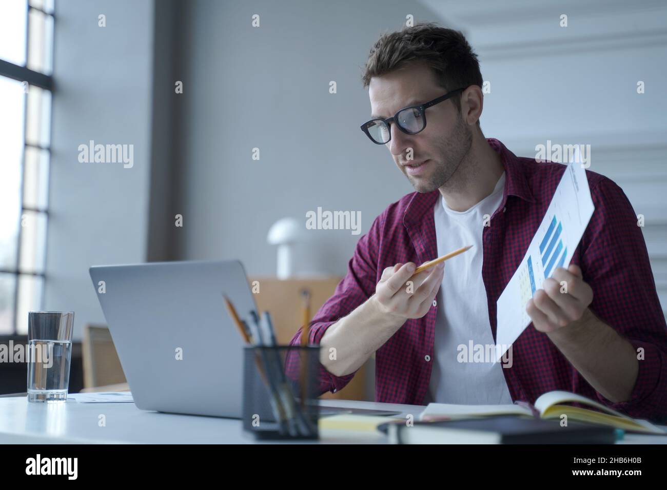 Jeune travailleur de bureau européen en lunettes montrant un rapport statistique pendant la réunion en ligne Banque D'Images