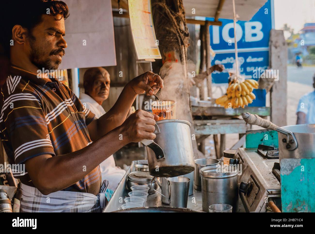 Tamil Nadu, Inde - 14 janvier 2016.Un homme prépare une casserole de thé chai à un stand de nourriture en bord de route, à la lumière du matin. Banque D'Images