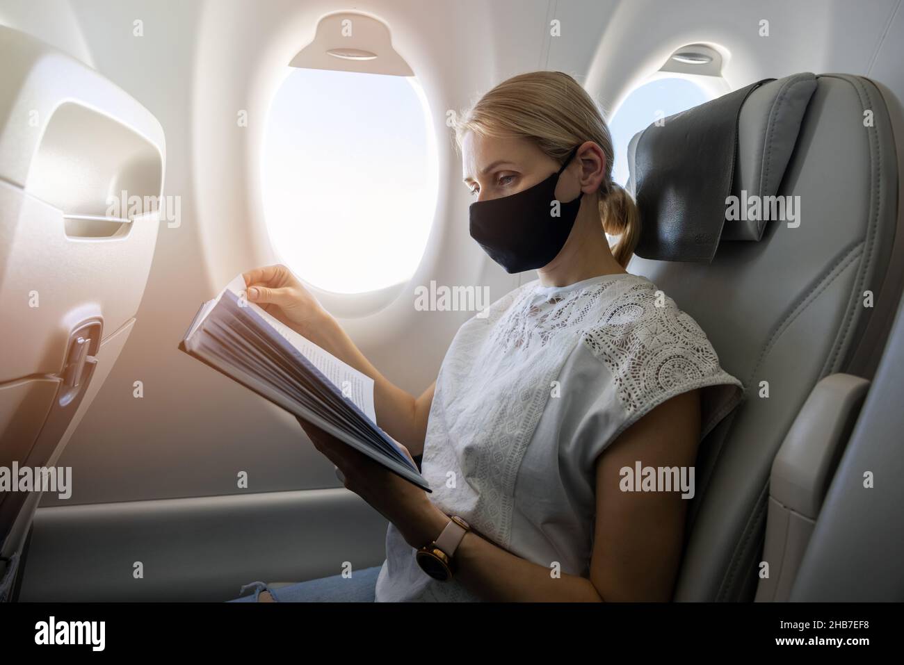femme portant un masque facial et un livre de lecture en avion. voyage en cas de pandémie Banque D'Images