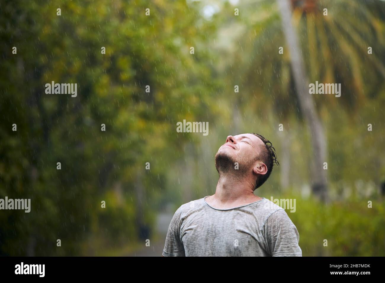 Portrait d'un homme trempé avec les yeux fermés et bénéficiant d'une forte pluie dans la nature. Banque D'Images