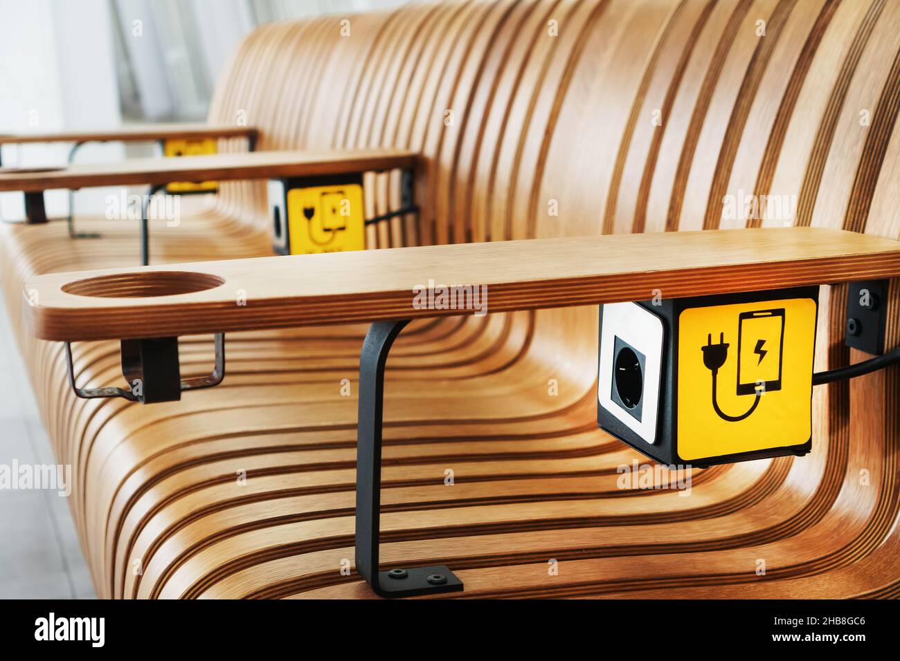 Un banc en bois design avec prises et un panneau jaune pour charger les smartphones dans la salle d'attente.Sans fil, fiche Banque D'Images