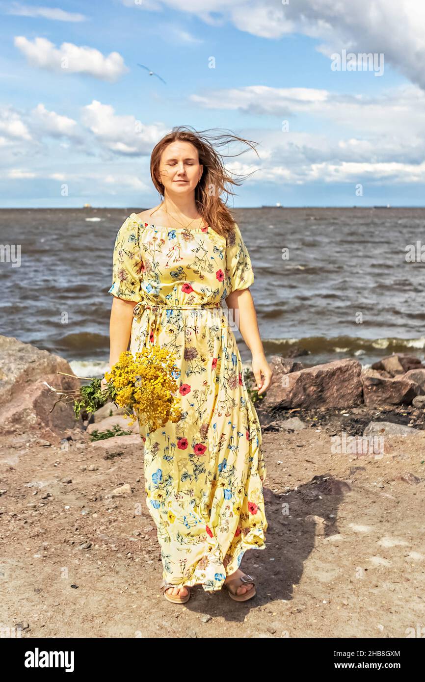 Une jeune femme vêtue d'une robe jaune avec un bouquet de tansy se dresse  sur la plage au vent.Clair et aéré Photo Stock - Alamy