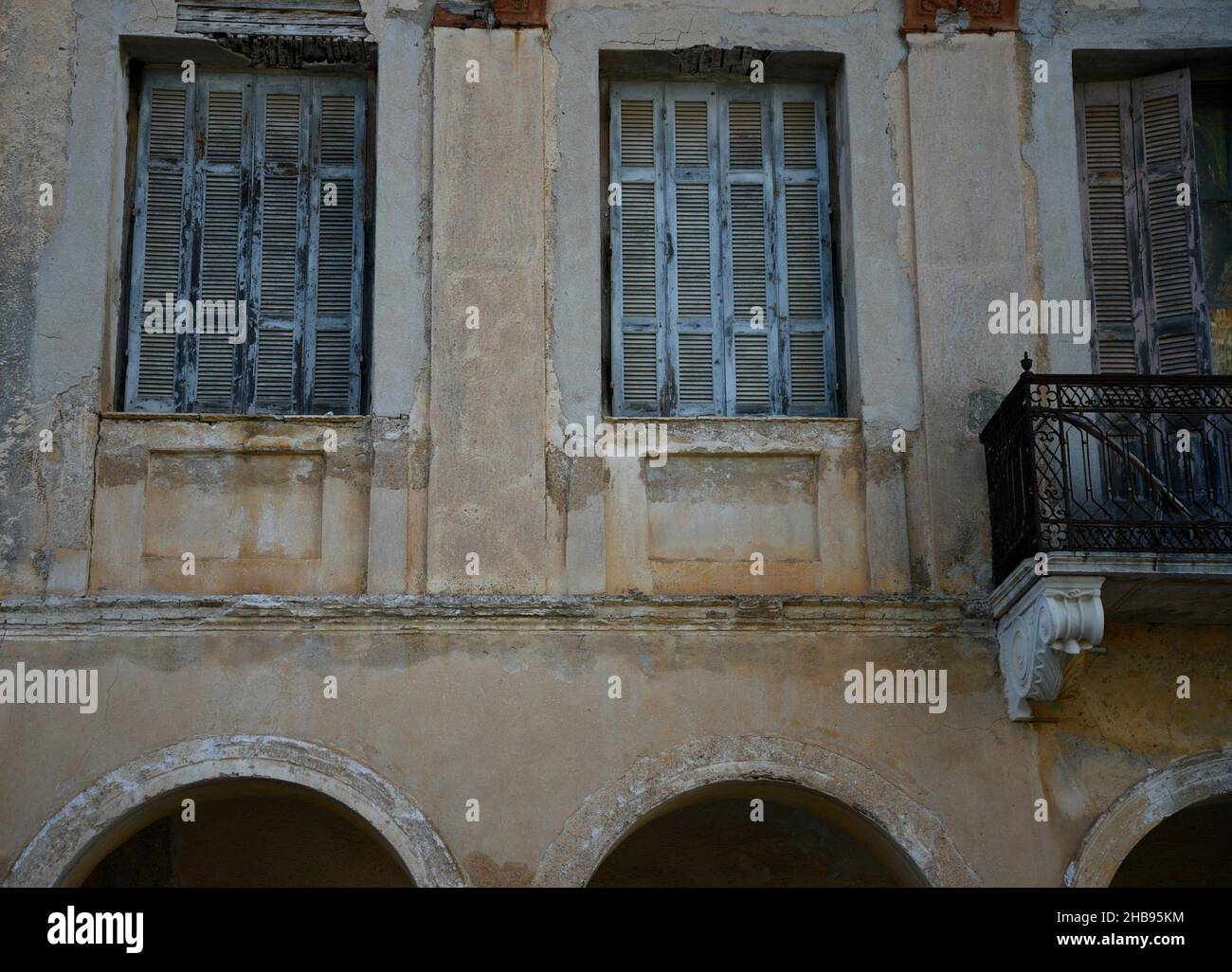 Ancienne façade de maison rurale traditionnelle avec un mur de stuc patiné, des volets de fenêtre en bois bleu clair et une balustrade de balcon en fer rouillé à Koroni, Grèce. Banque D'Images