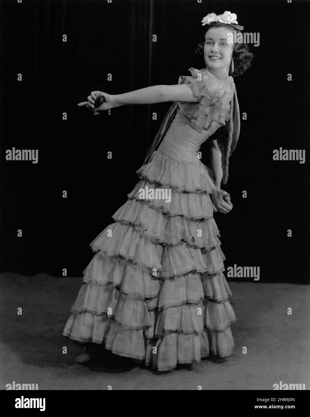 Jeune femme habillée en robe pleine longueur avec des couches de volants dansant avec des castanets.Vers 1945 Banque D'Images