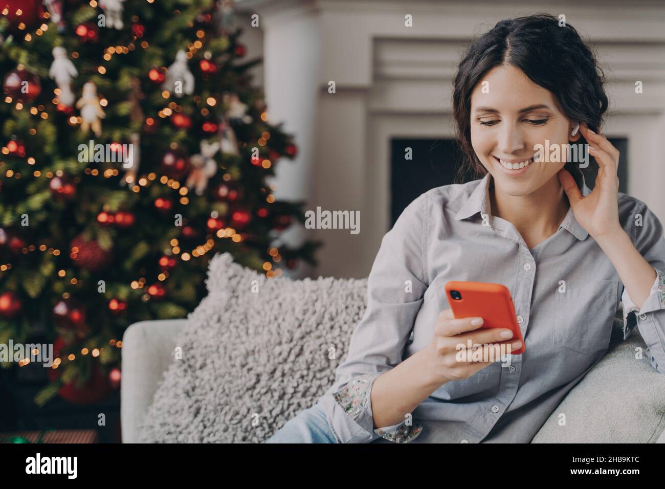 Décontractée heureuse italienne femme assise dans un canapé confortable à la maison avec téléphone pendant les vacances de Noël Banque D'Images