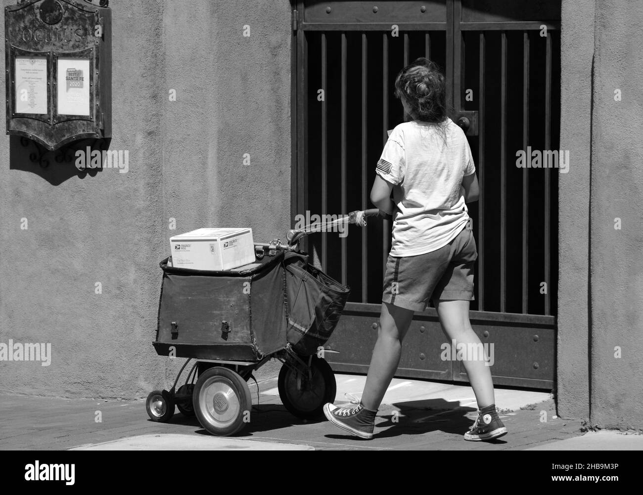 Une travailleuse postale livre le courrier et les colis dans le centre-ville de Santa Fe, au Nouveau-Mexique, à l'aide d'un chariot à roues. Banque D'Images