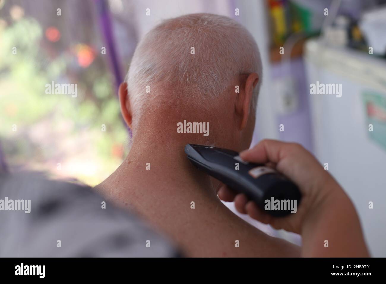 Beau homme âgé qui se coiffe.Personne âgée qui coupe ses cheveux à l'aide d'une tondeuse électrique. Banque D'Images
