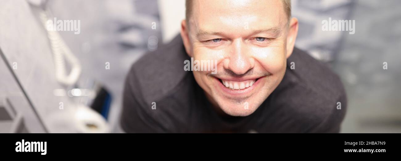 Portrait d'un jeune homme content assis sur les toilettes à proximité Banque D'Images
