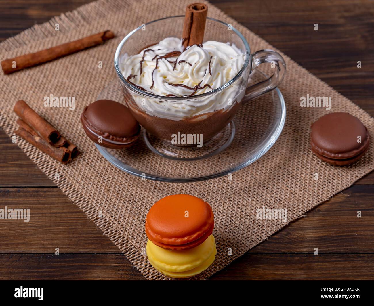 Une tasse de verre avec du chocolat chaud et de la crème sur une table avec quelques macarons colorés Banque D'Images