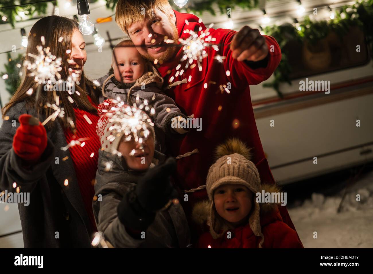 Une grande famille heureuse fête noël dans la nature et accueille des amateurs de sparkers.Les parents avec trois fils voyagent dans une maison mobile. Banque D'Images