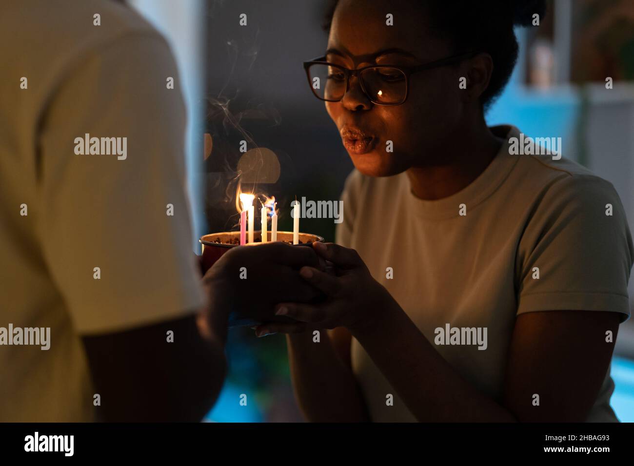 Jeune femme africaine heureuse soufflant des bougies sur un gâteau cuit par un mari bien-aimé pour l'anniversaire Banque D'Images