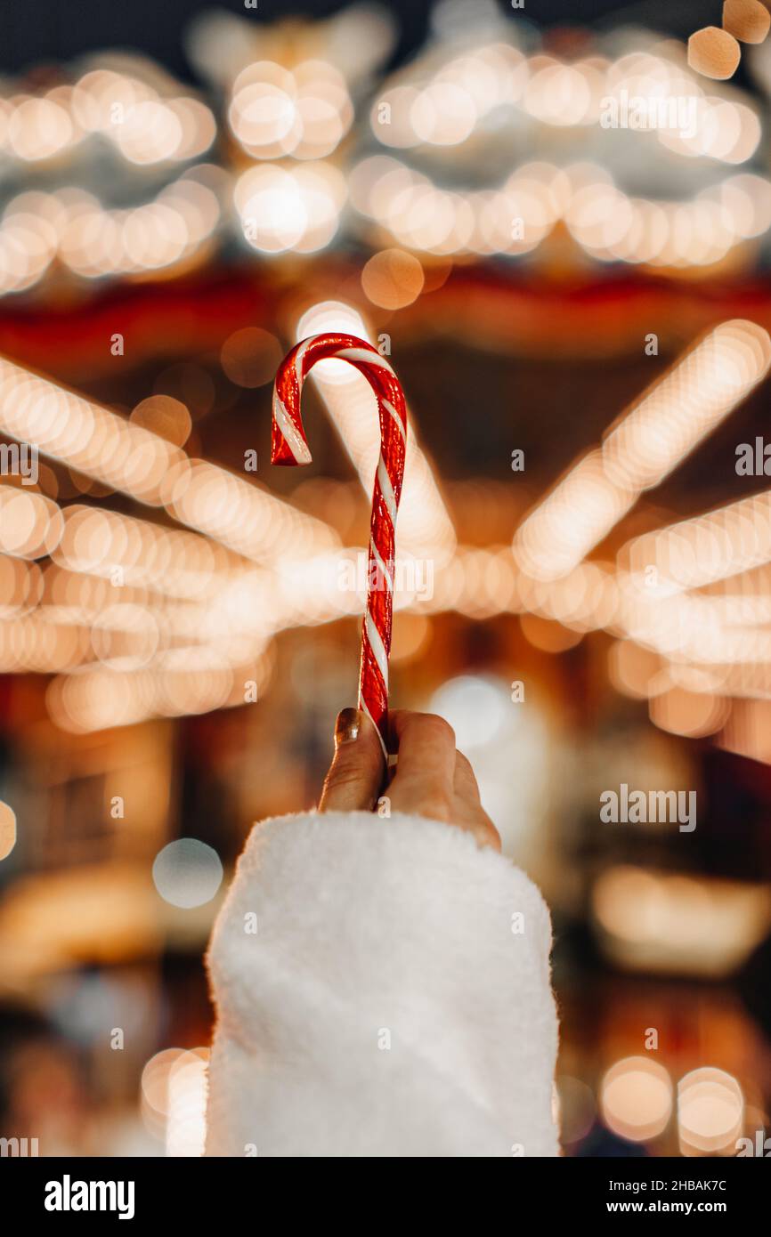 Main femelle tenant rouge blanc canne douce lollipop sur le fond des lumières de fée d'or.Détails magiques de Noël Banque D'Images
