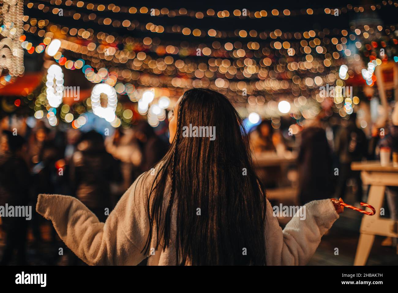 Jeune femme brune en fourrure blanche d'hiver au marché de Noël avec des lumières magiques dorées Banque D'Images