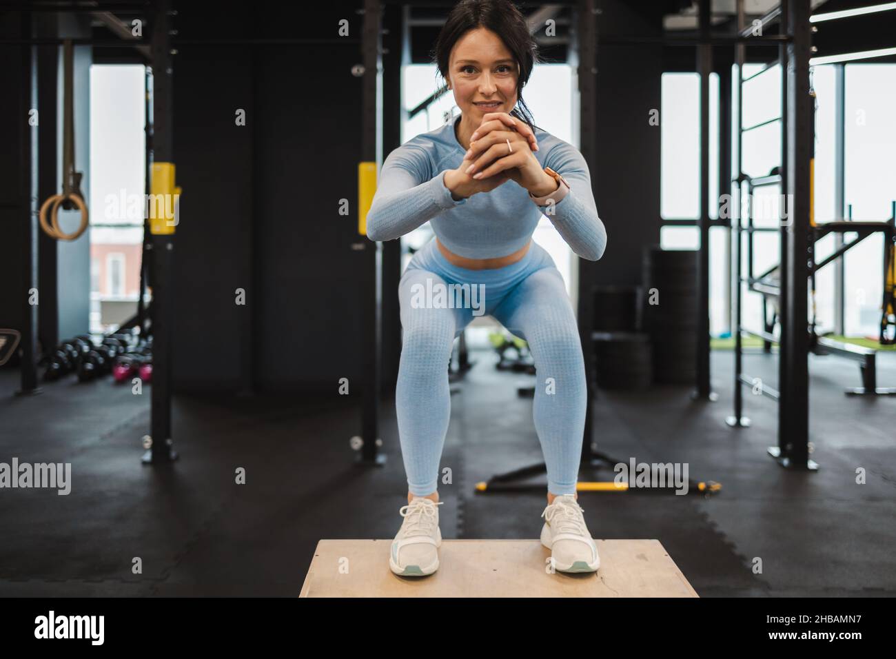 Vue de face d'une femme athlétique dans un vêtement de sport bleu faisant  du squat tout en se tenant sur une boîte crossfit en bois à la salle de  sport Photo Stock -