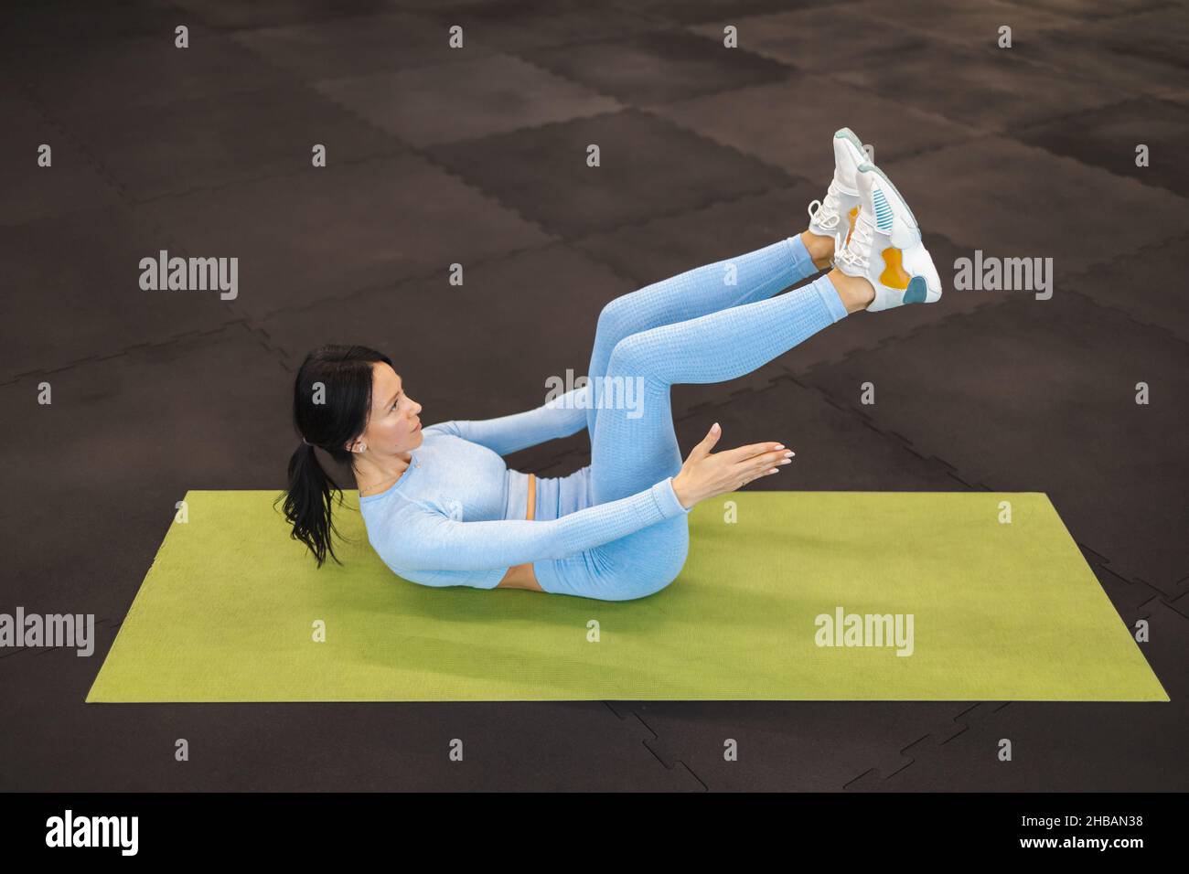 Une jeune fille de forme physique qui se trouve sur le sol de la salle de gym secoue l'abs en levant les jambes Banque D'Images