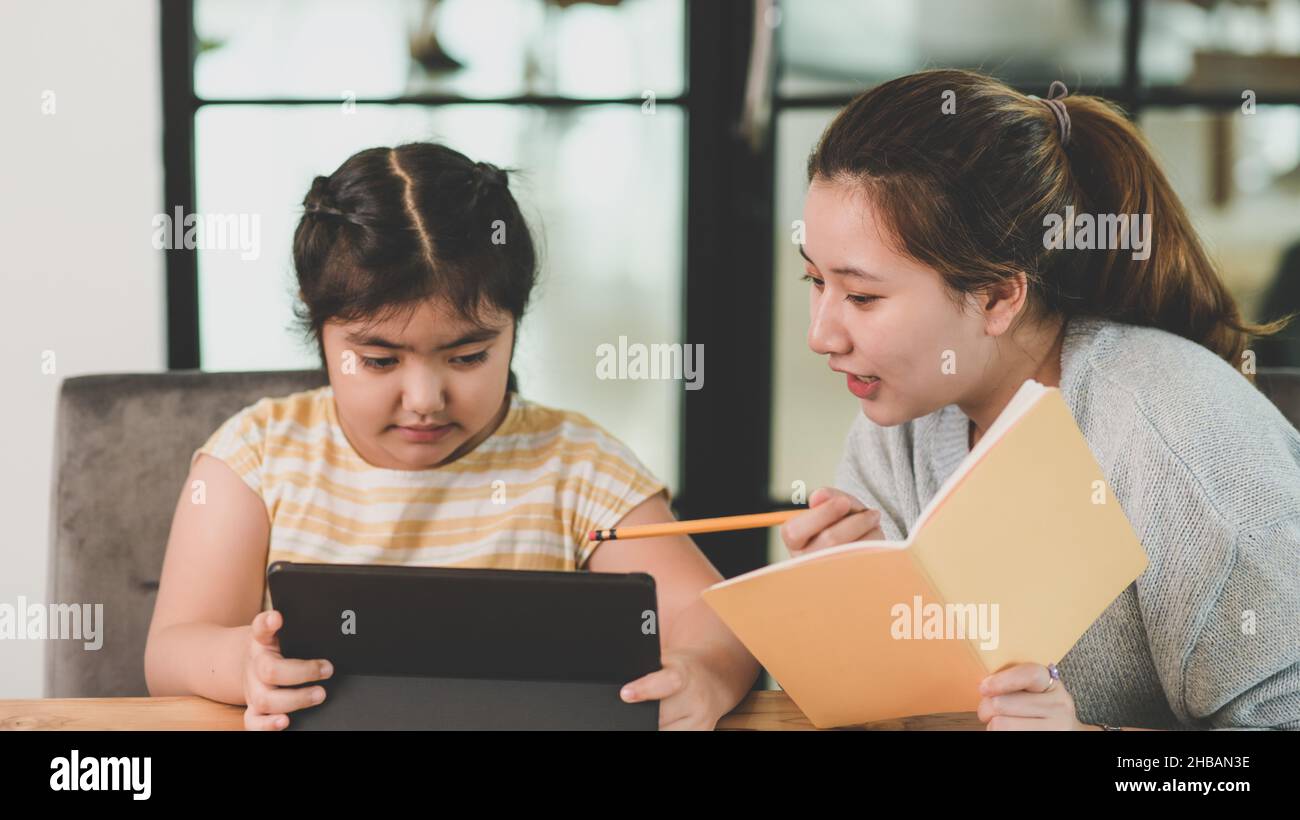 Enseignement pédagogique, devoirs enfant fille regardant la tablette, enfant asiatique fille étudiant en ligne avec la tablette, soeur enseignant soeur pour faire les devoirs. Banque D'Images