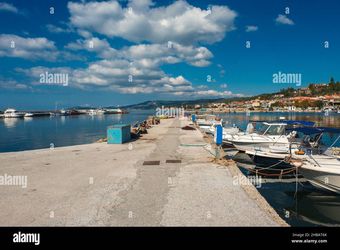 Quai en béton avec des navires ancrés et des bateaux sous un ciel bleu nuageux par une journée ensoleillée Banque D'Images