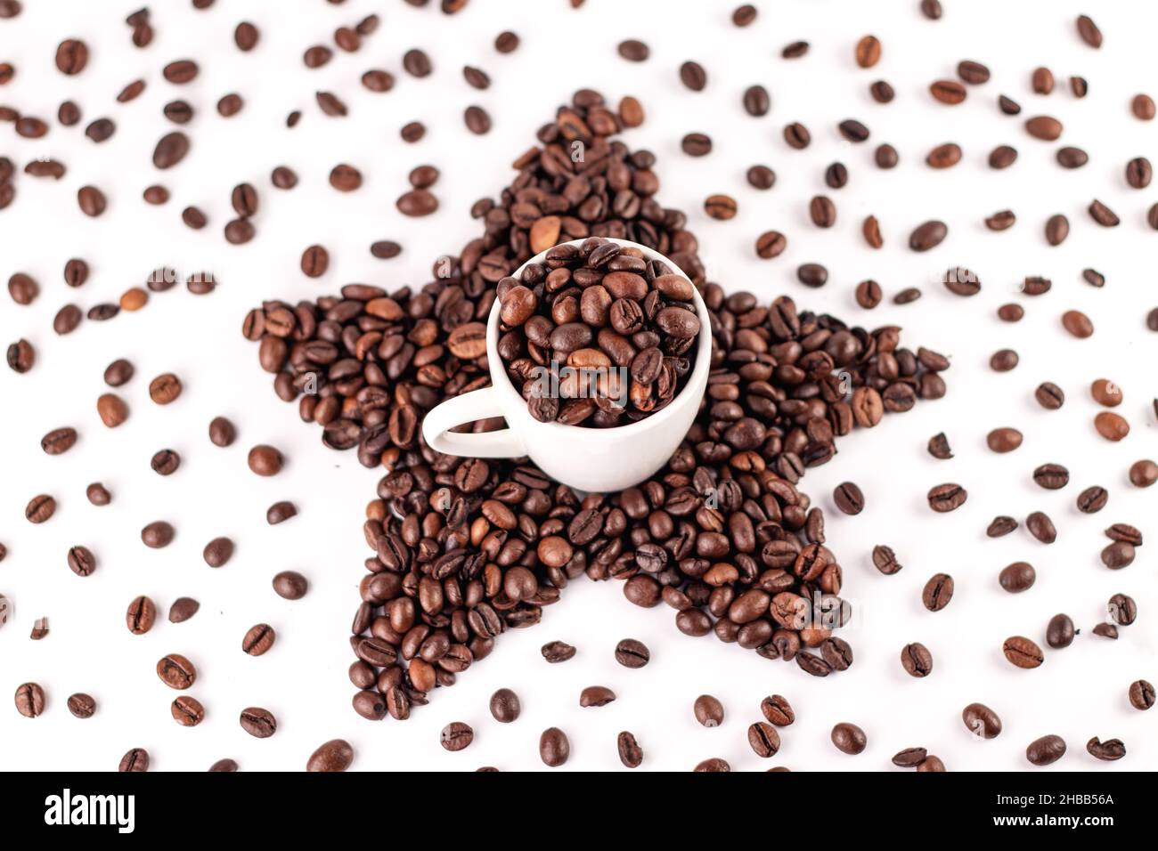 Tasse de café et étoile à base de grains de café torréfiés sur fond blanc.Grains de café épars. Banque D'Images