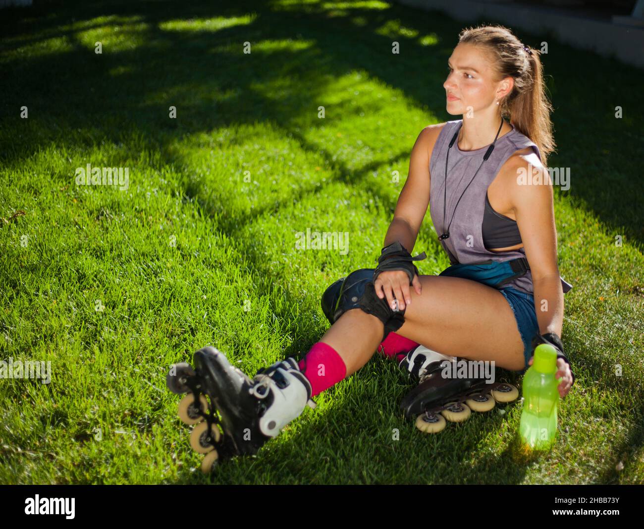 Une jeune femme en équipement de protection et des patins à roulettes est assise dans le parc sur l'herbe.Le concept des activités de plein air.Passe-temps.Style de vie sportif Banque D'Images
