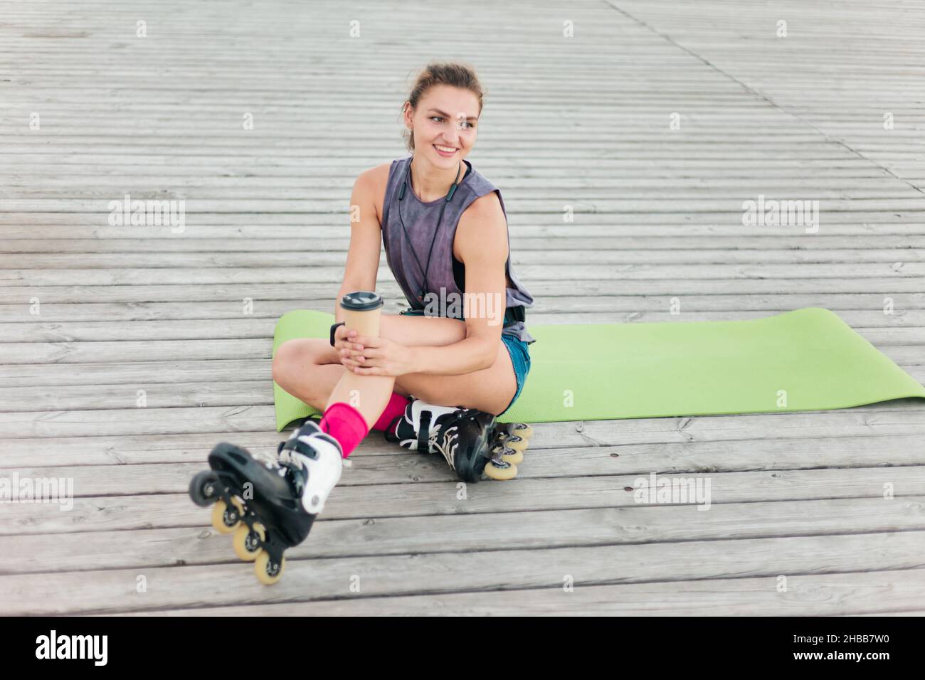 Jeune femme heureuse patineuse à roulettes sittinп sur tapis à l'extérieur.Style de vie sportif Banque D'Images