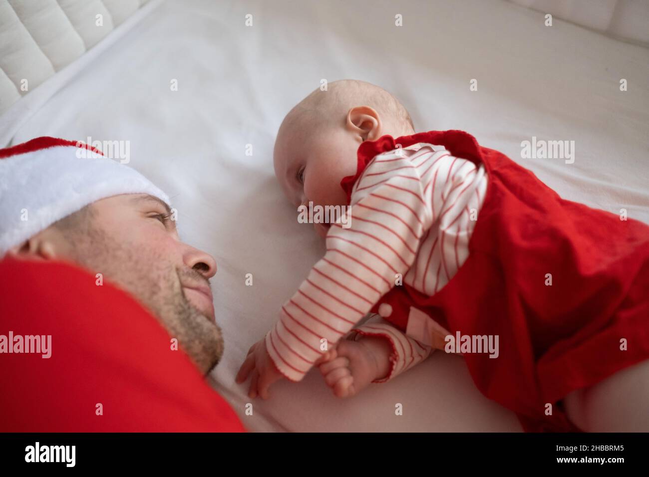 Père avec sa petite fille en robe de Noël reposant sur le lit. Banque D'Images