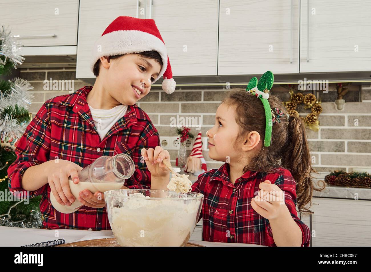 Adorables enfants européens qui apprécient le temps ensemble, qui s'amusent tout en pétriant de la pâte, en cuisant des biscuits et des boulangeries, aidant leur mère à la cuisine Banque D'Images