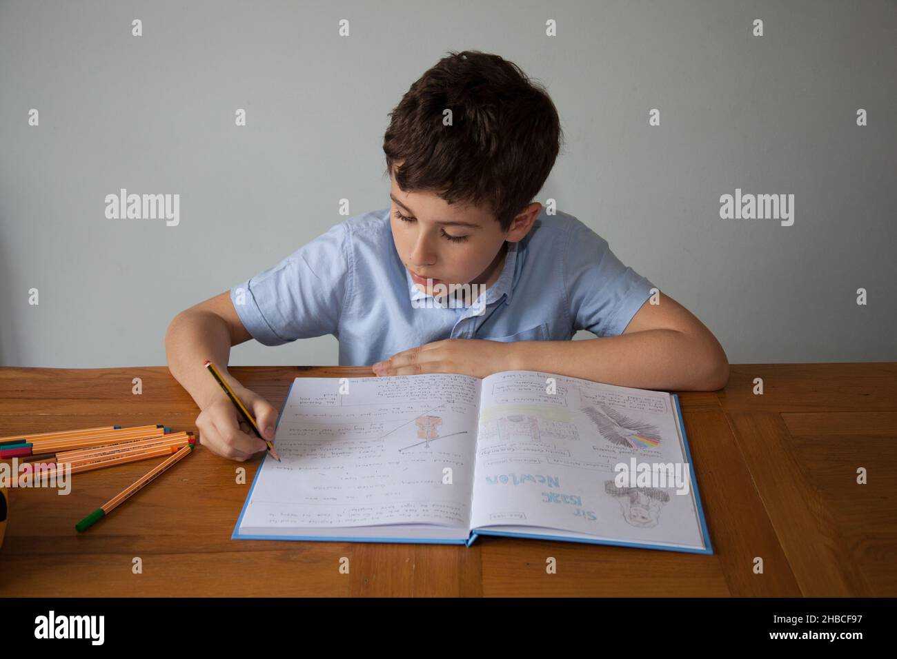 Un garçon d'école, âgé de 11 ans, faisant quelques devoirs avec un livre ouvert contenant des écrits et des dessins Banque D'Images